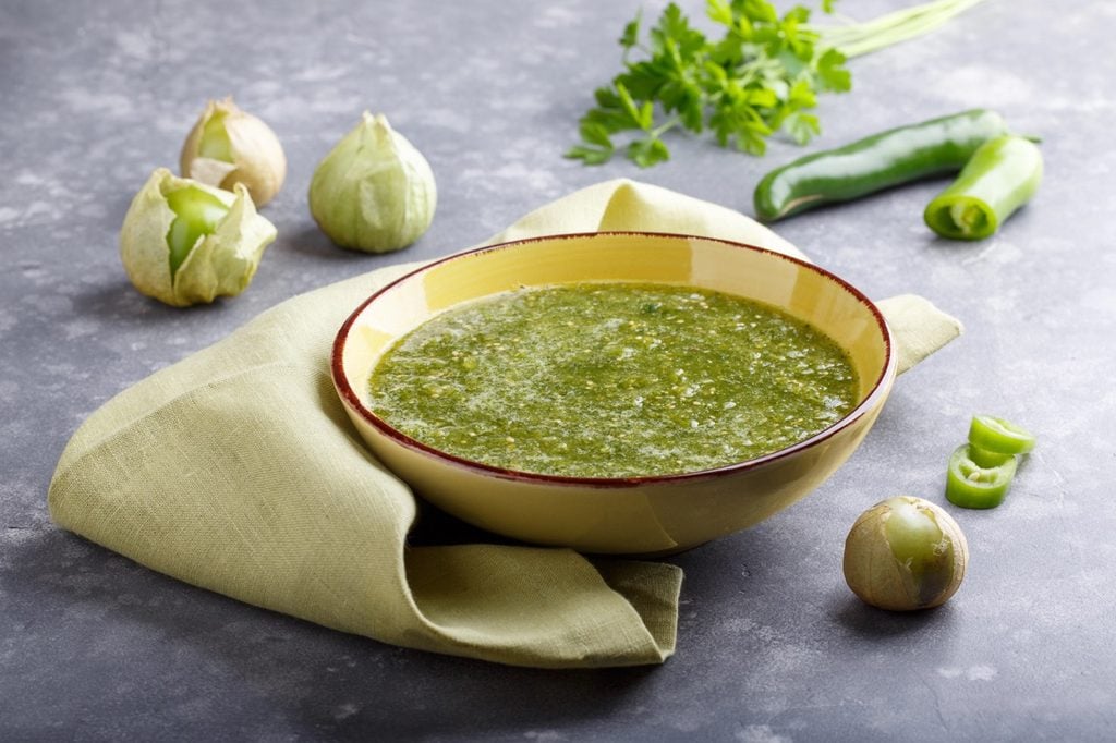 Salsa verde on a table surrounded by tomatillos and chili peppers.