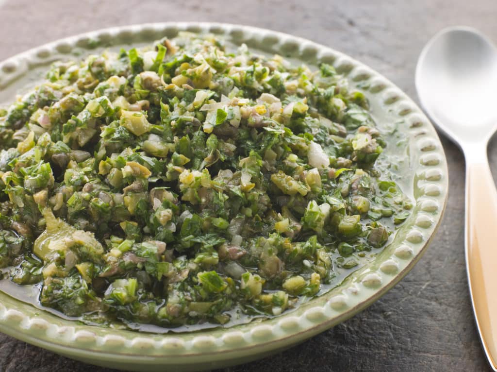 A plate of chunky herb salsa verde made with chopped parsley, capers and olive oil