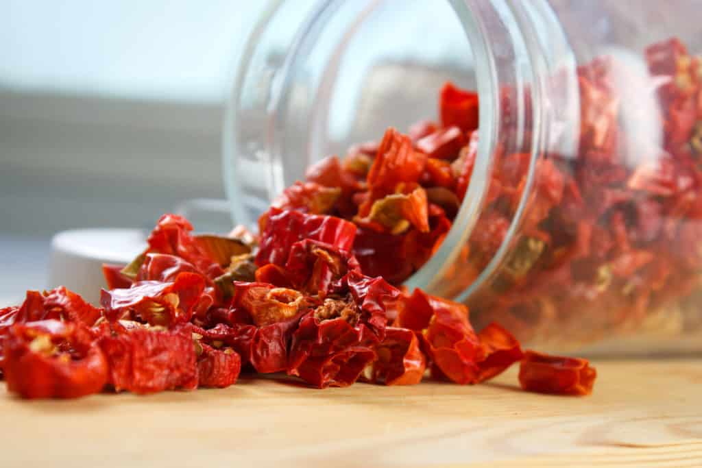Dried red chili pepper pieces spilling out of a glass jar