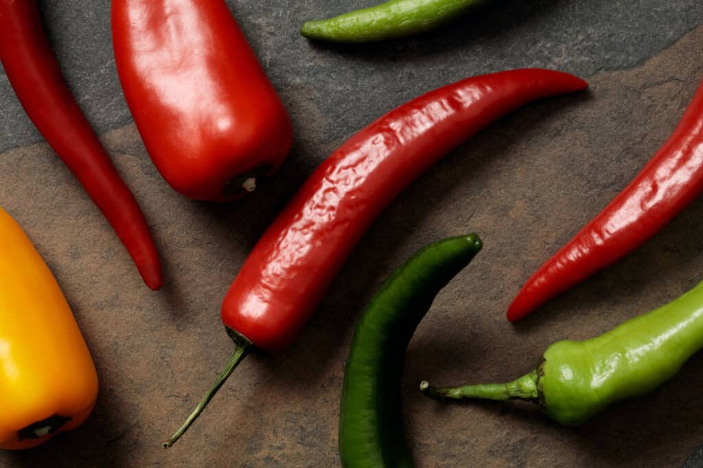 Red and green chili peppers and a piece of yellow bell pepper on a dark stone surface